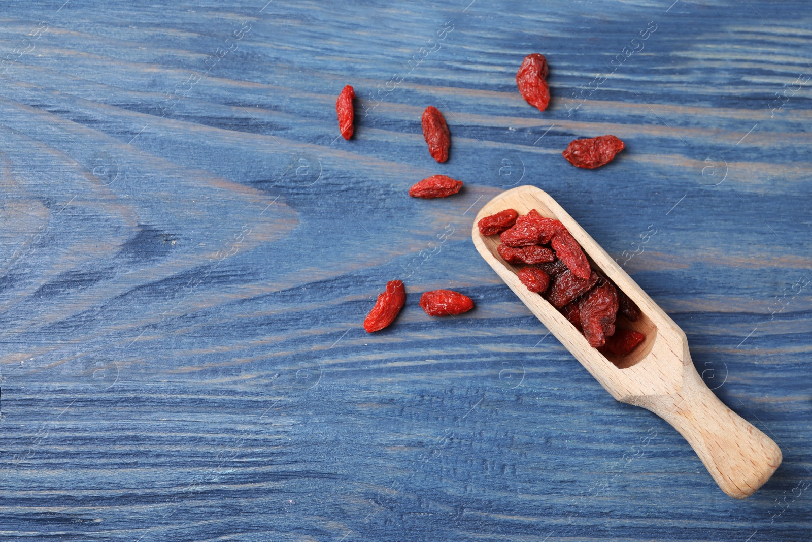 Photo of Dried goji berries on blue wooden table, flat lay. Space for text