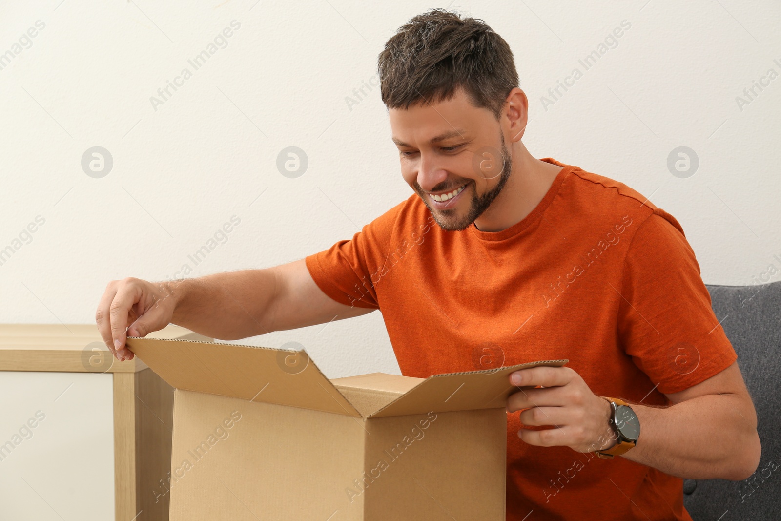 Photo of Happy man opening parcel indoors. Internet shopping