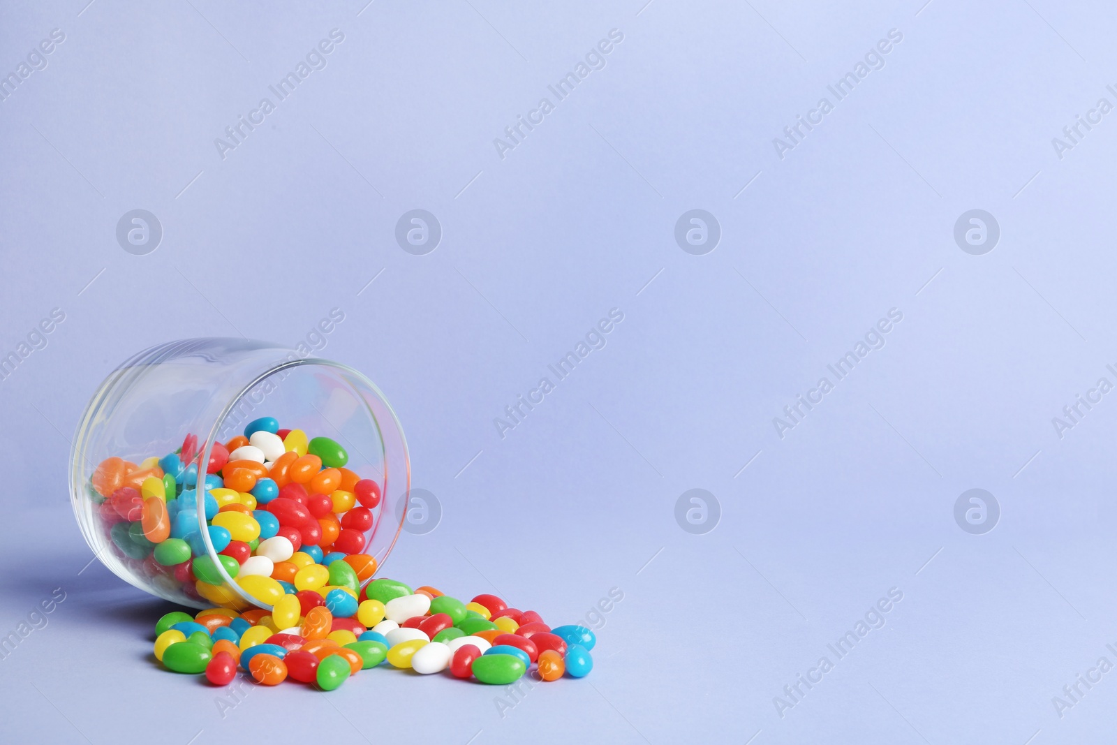 Photo of Glass jar with delicious bright jelly beans on color background. Space for text