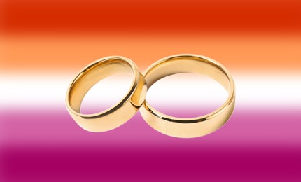 Golden wedding rings on background in color of lesbian flag