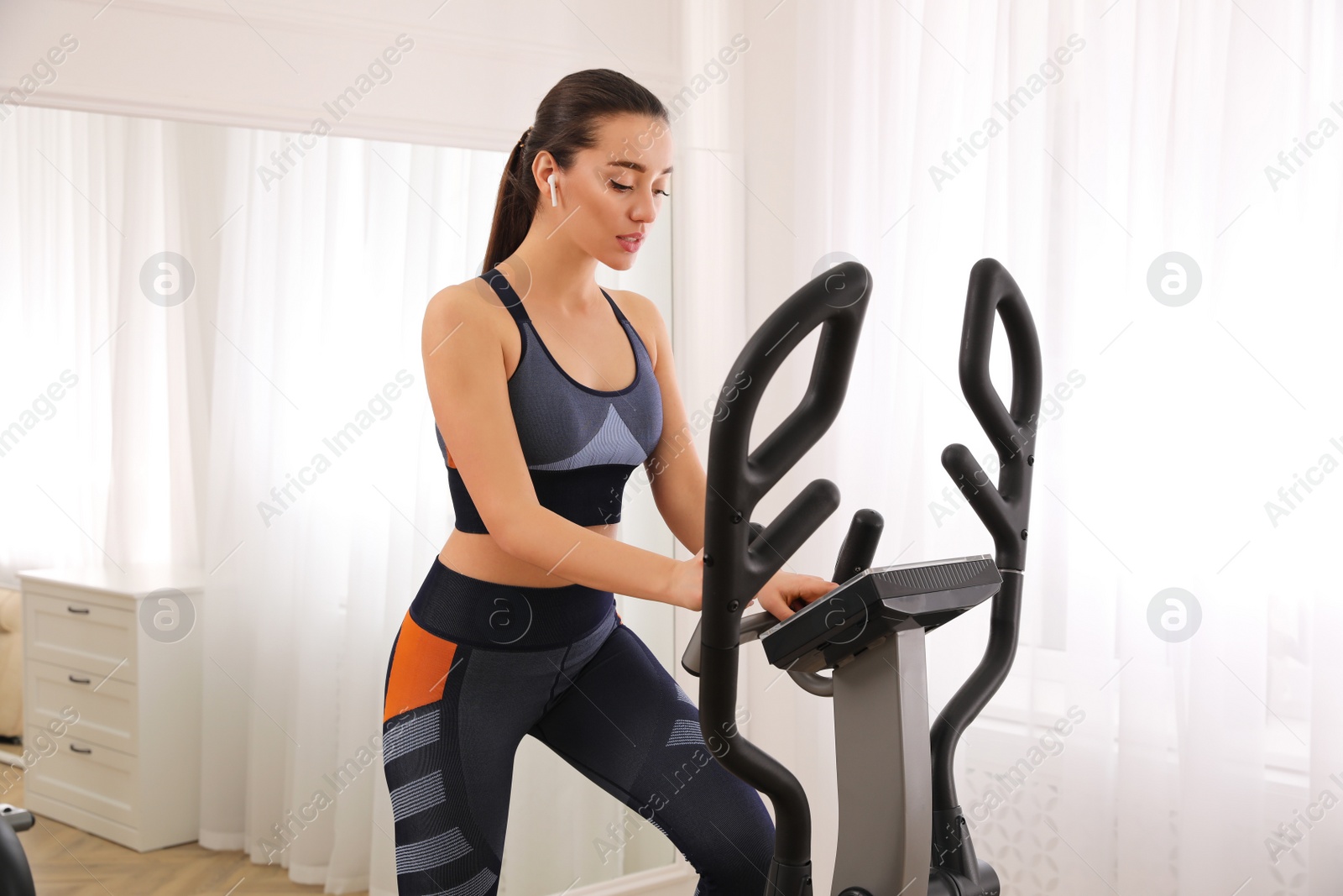 Photo of Woman using modern elliptical machine at home