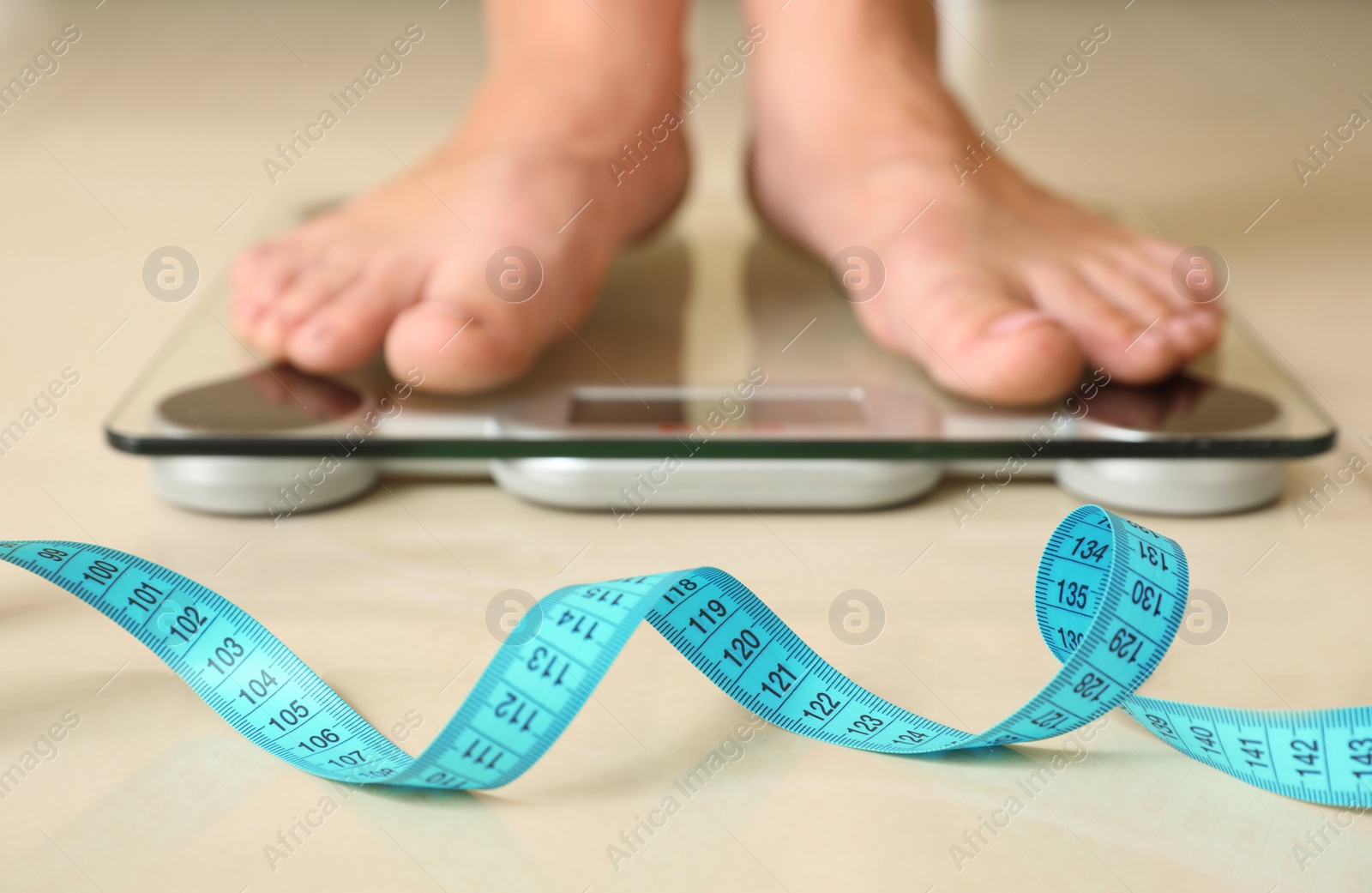 Photo of Tape in front of woman standing on floor scales indoors. Overweight problem