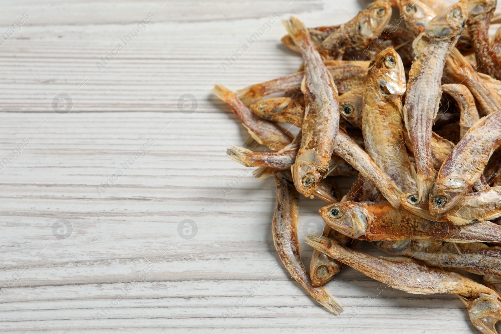 Photo of Heap of tasty dried anchovies on white wooden table, closeup. Space for text