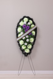 Photo of Funeral wreath of plastic flowers near grey wall indoors