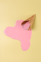 Photo of Melted ice cream and wafer cone on pale yellow background, top view