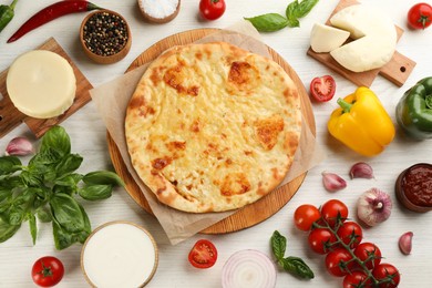 Photo of Delicious khachapuri with cheese surrounded by different products on white wooden table, flat lay