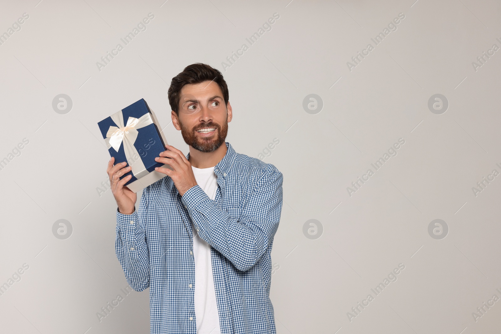 Photo of Emotional man holding gift box on light grey background, space for text