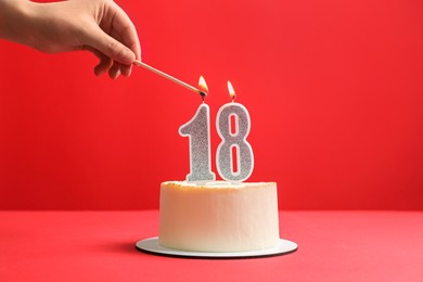 Coming of age party - 18th birthday. Woman lighting number shaped candles on cake against red background