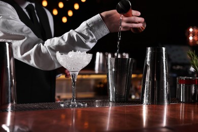 Bartender preparing fresh alcoholic cocktail in martini glass at bar counter, closeup