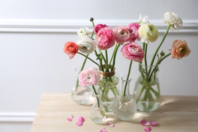Photo of Beautiful ranunculus flowers on wooden table near wall. Space for text