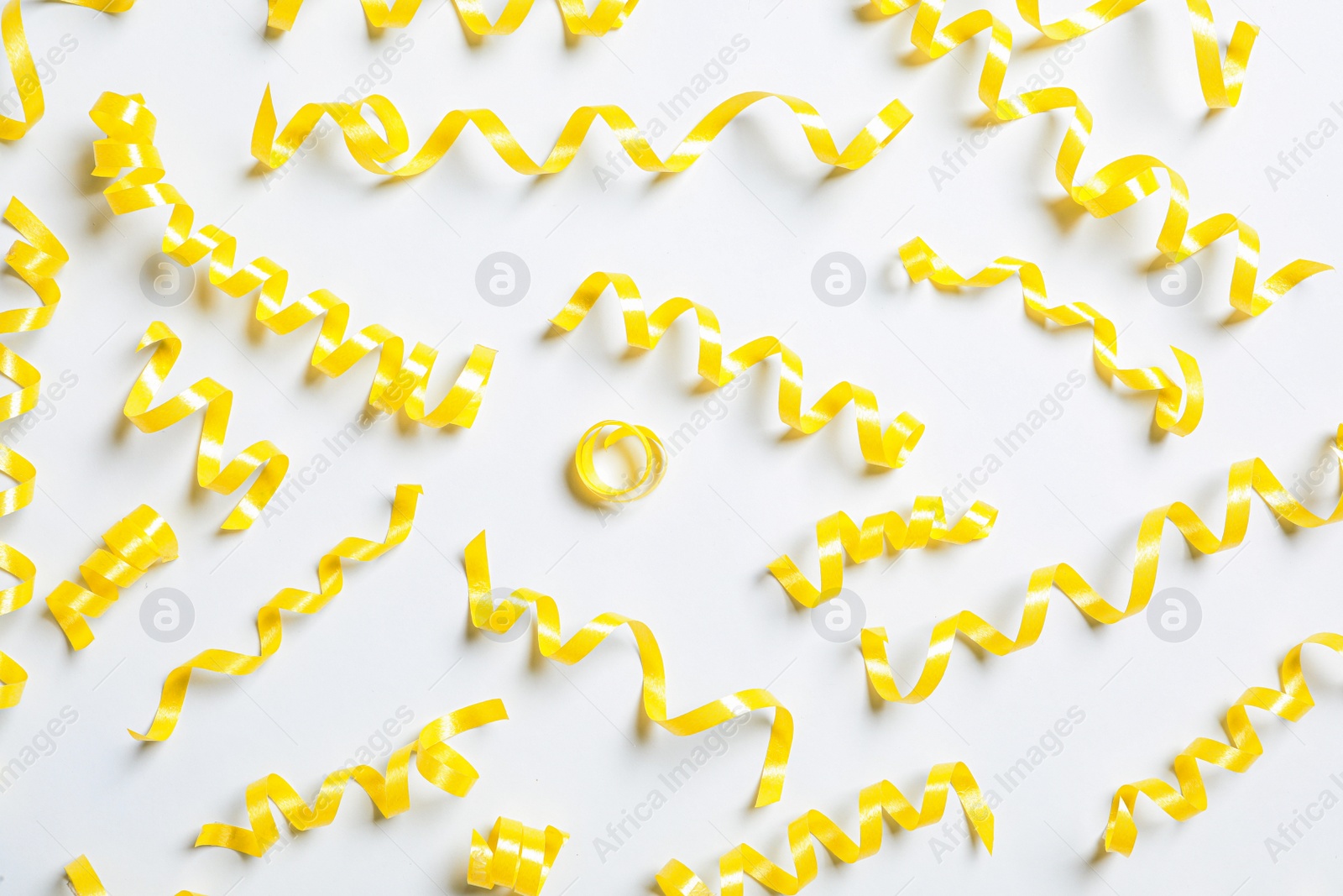 Photo of Yellow serpentine streamers on white background, top view