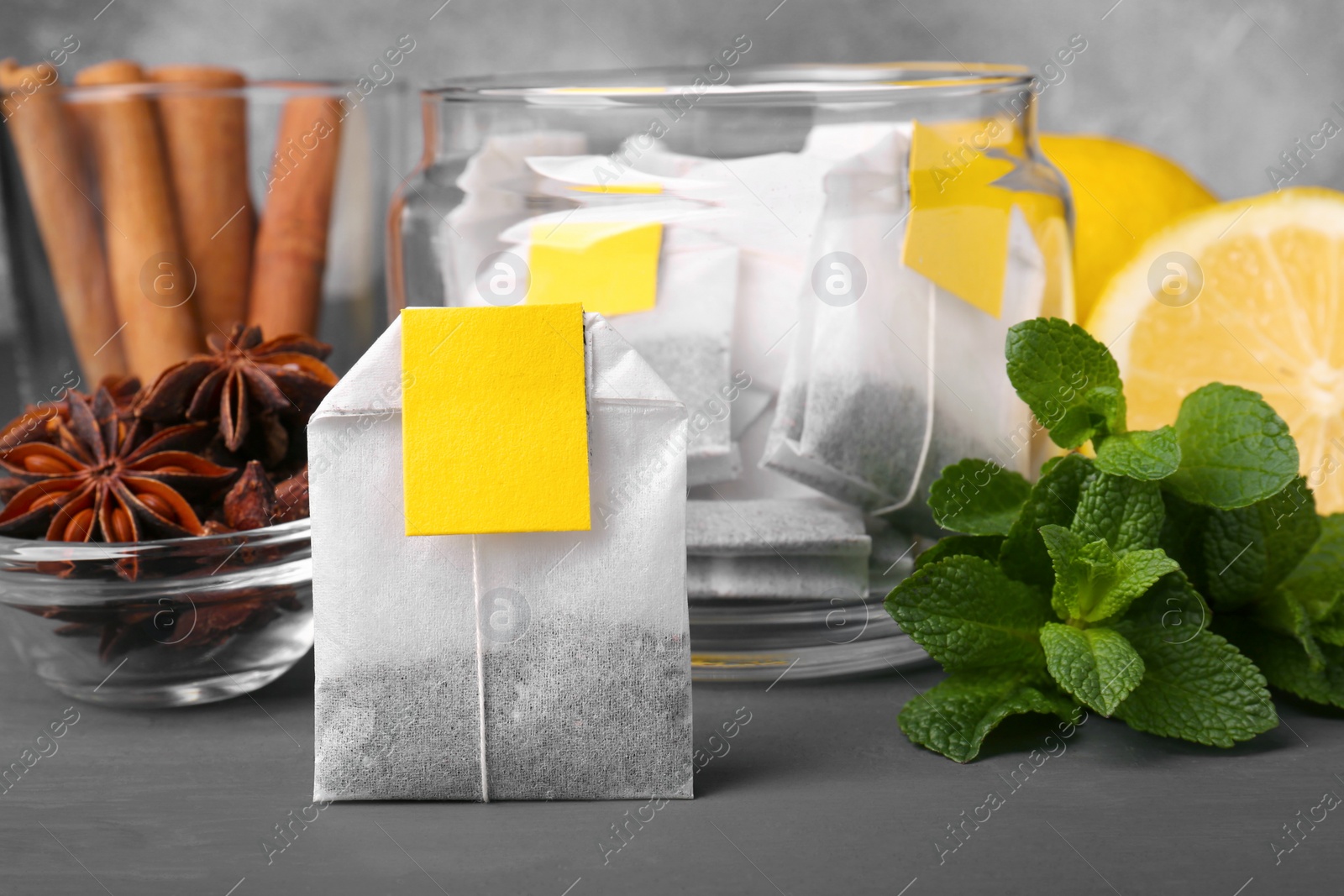 Photo of Tea bags, anise stars, cinnamon sticks, mint and lemon on grey table, closeup