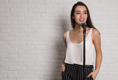 Photo of Young woman in casual clothes posing with microphone near brick wall. Space for text