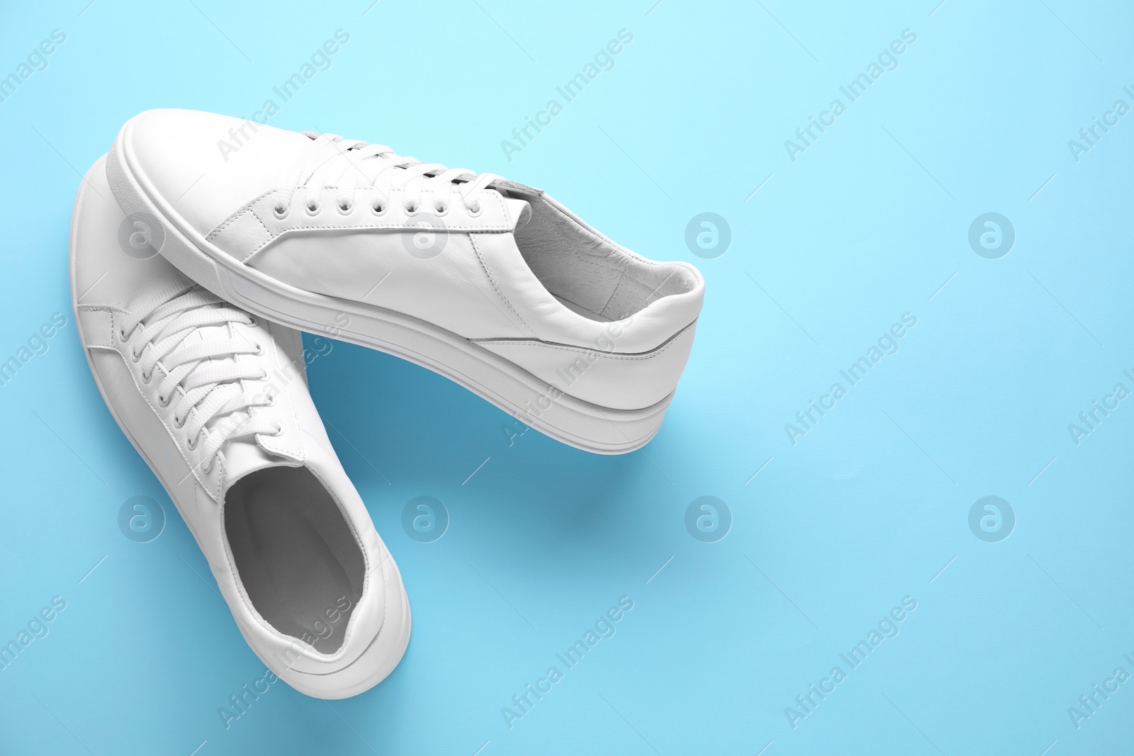 Photo of Pair of stylish white sneakers on light blue background, top view. Space for text