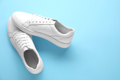 Pair of stylish white sneakers on light blue background, top view. Space for text