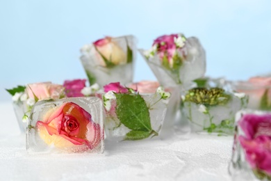 Ice cubes with flowers on table against color background