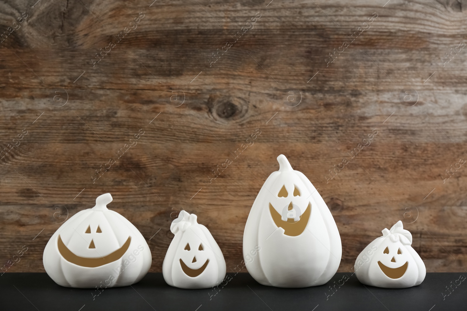 Photo of Jack-o-Lantern candle holders on black table against wooden background, space for text. Halloween decor
