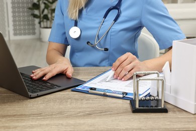 Doctor working with results of laboratory test and laptop at wooden table in clinic, closeup