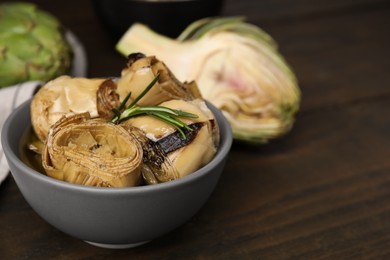 Photo of Bowl with delicious artichokes pickled in olive oil on wooden table, closeup. Space for text