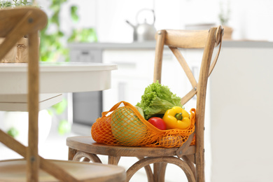 Photo of Net bag with vegetables on wooden chair in kitchen
