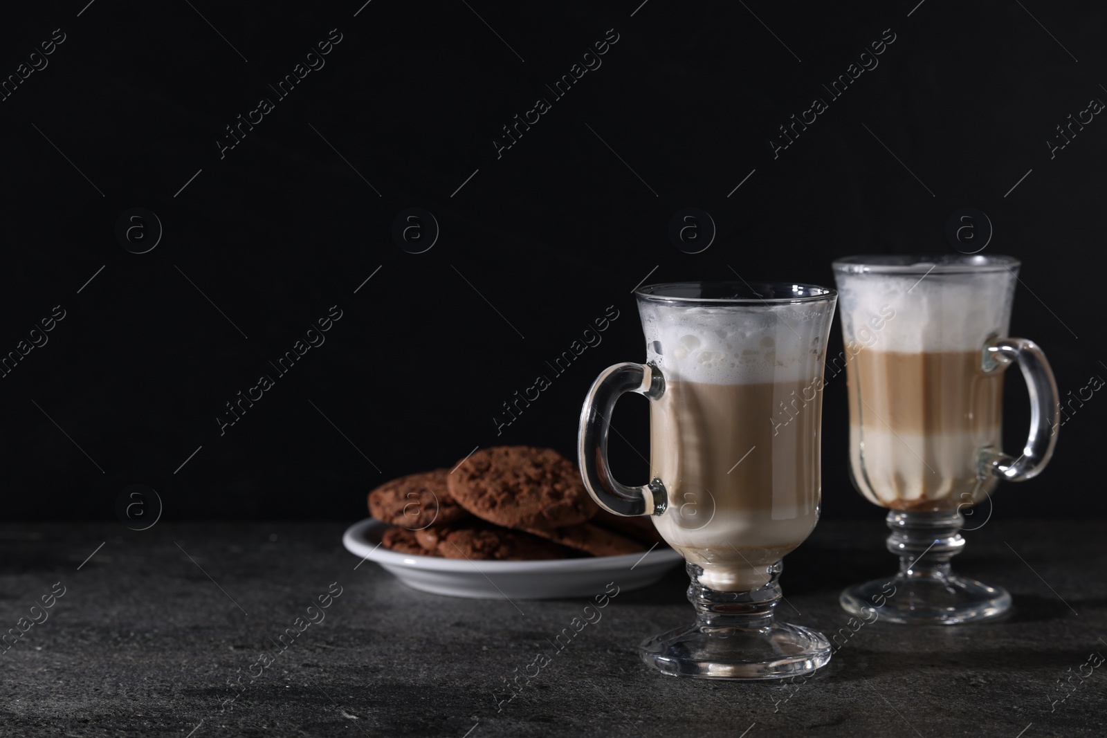 Photo of Aromatic latte macchiato in glasses and chocolate cookies on dark grey table. Space for text