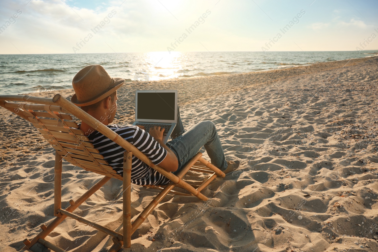 Photo of Man working with laptop in deck chair on beach