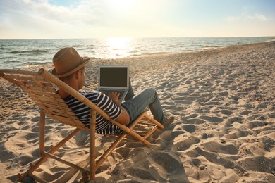 Man working with laptop in deck chair on beach