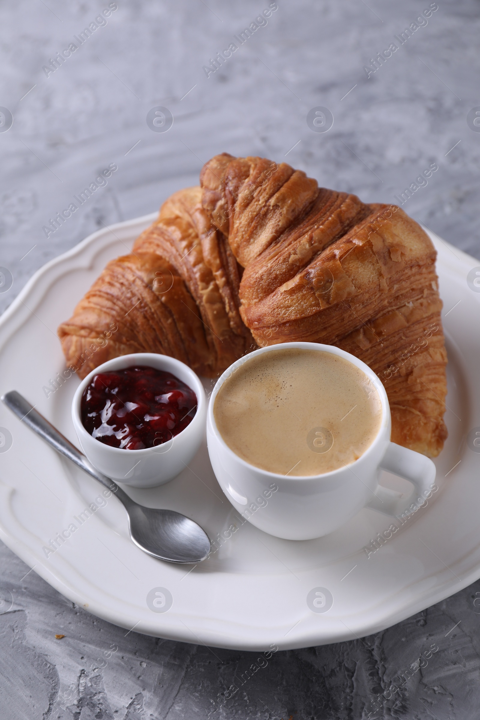 Photo of Tasty breakfast. Cup of coffee, fresh croissants and jam on grey table