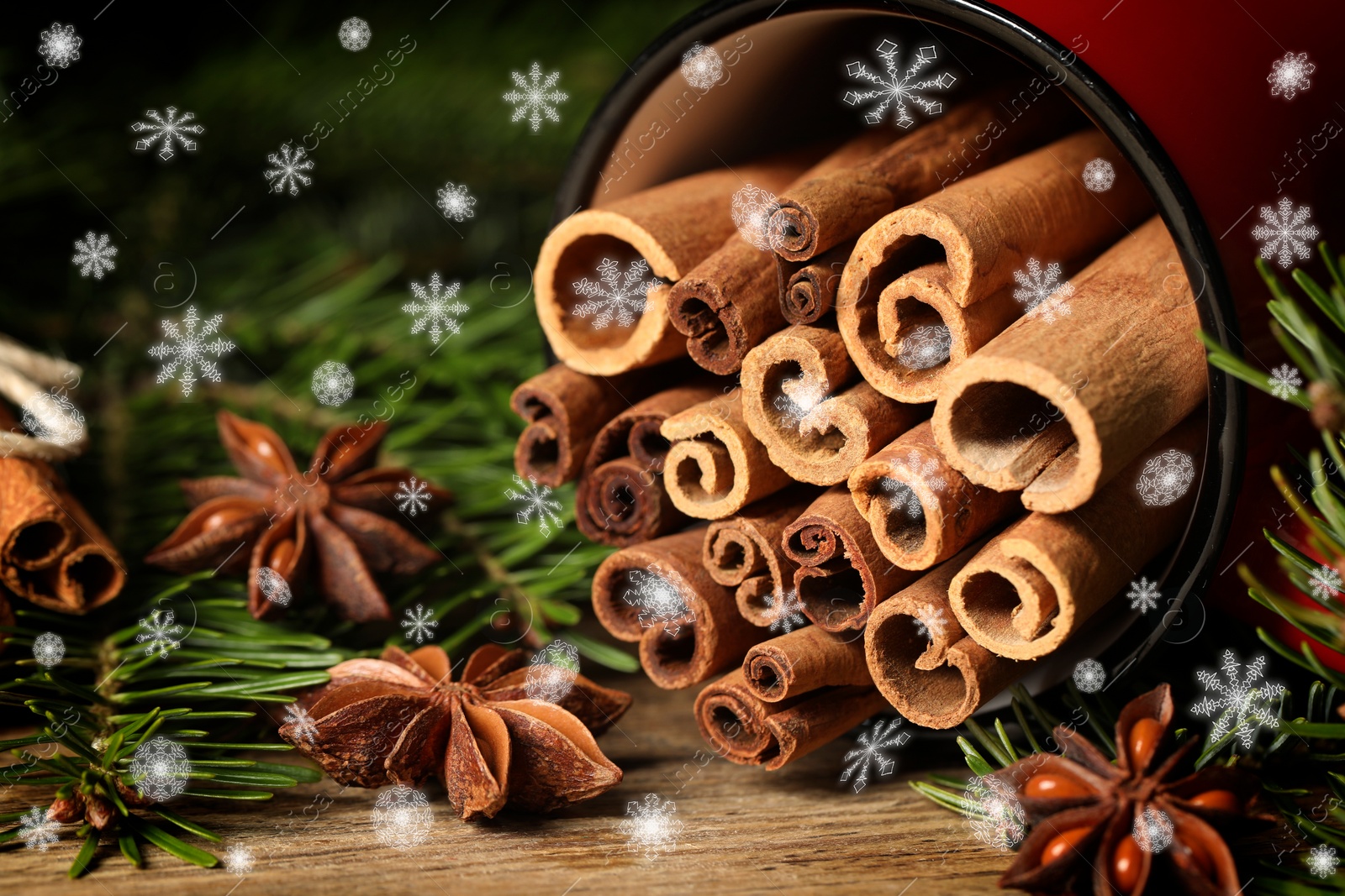 Image of Cinnamon in red mug and anise surrounded by fir tree branches on wooden table, closeup