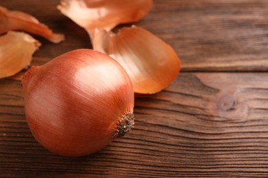 Photo of Fresh ripe onion on wooden table, closeup. Space for text