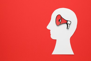 Photo of Top view of paper human head cutout with megaphone on red background, space for text. Hybrid war concept