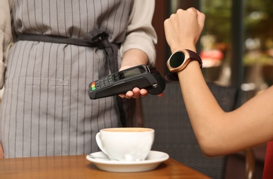 Woman making payment with smart watch in cafe, closeup