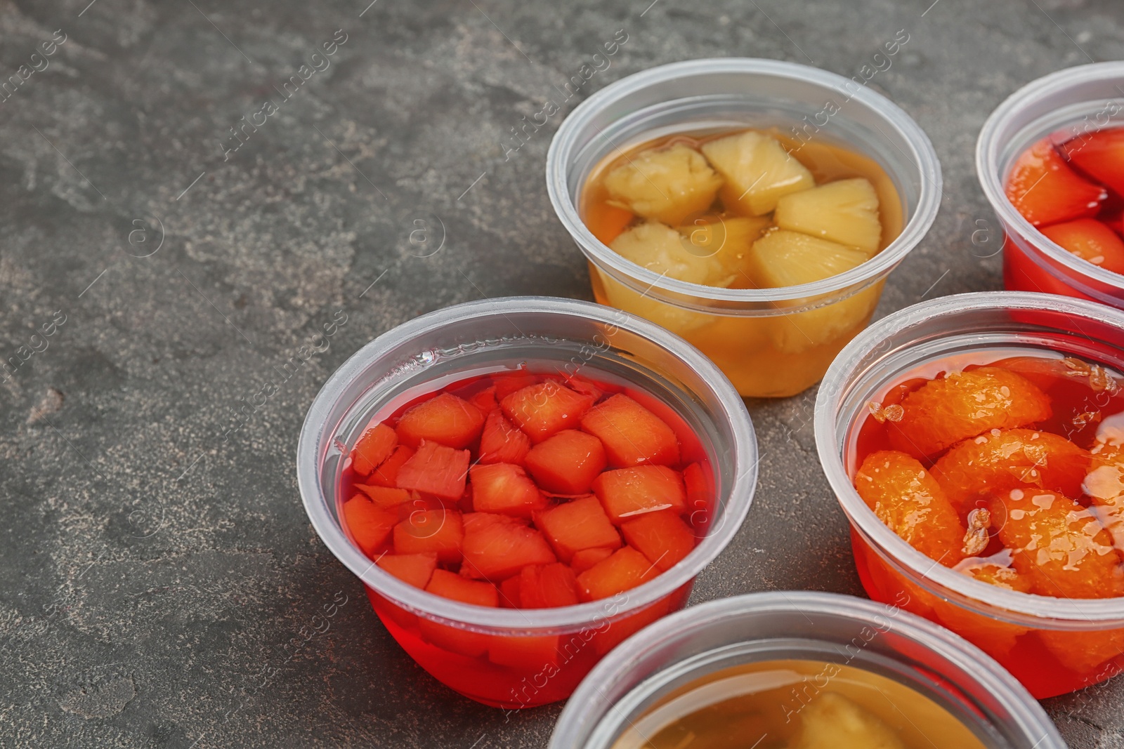 Photo of Plastic containers of tasty jelly desserts with fruit pieces on grey background