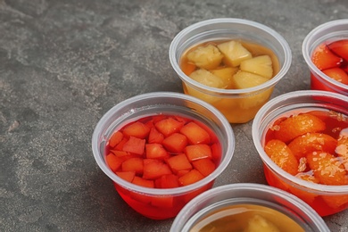 Plastic containers of tasty jelly desserts with fruit pieces on grey background