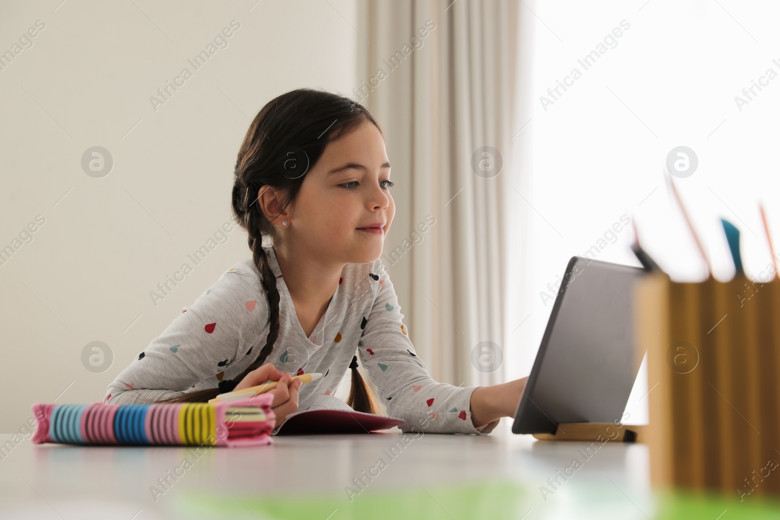 Photo of Little girl doing homework with modern tablet at home