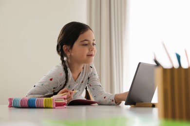 Little girl doing homework with modern tablet at home