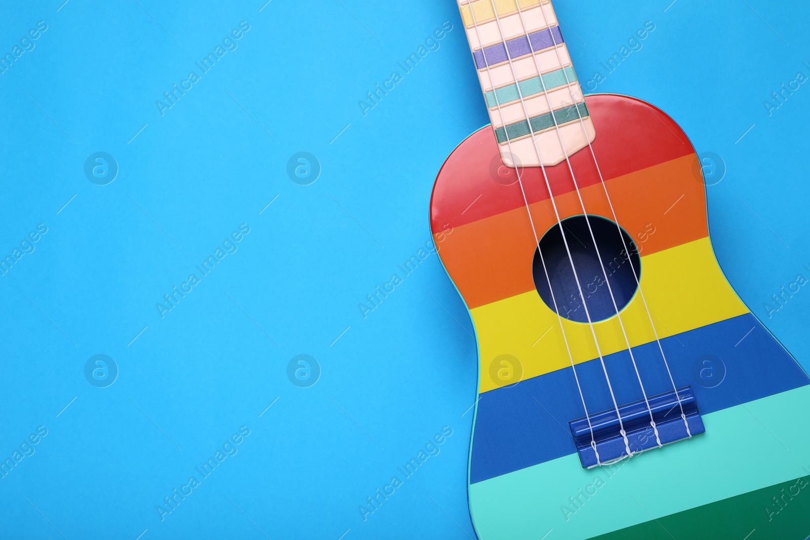 Photo of Colorful ukulele on light blue background, top view and space for text. String musical instrument