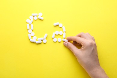 Photo of Woman making calcium symbol with white pills on yellow background, top view