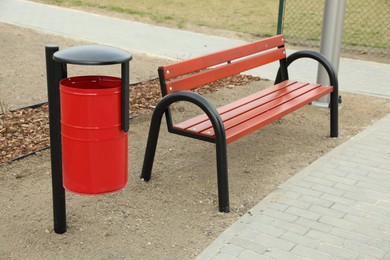 Photo of Red metal trash bin near wooden bench in city park