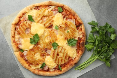 Photo of Delicious pineapple pizza and parsley on gray table, top view