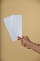 Man holding flyers on beige background, closeup. Mockup for design