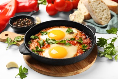 Photo of Delicious shakshuka in frying pan and products on white table, closeup