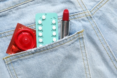 Closeup view of jeans with red lipstick and contraceptives in pocket. Safe sex concept