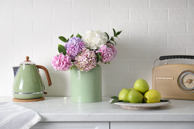 Beautiful hydrangea flowers, kettle and apples on light countertop