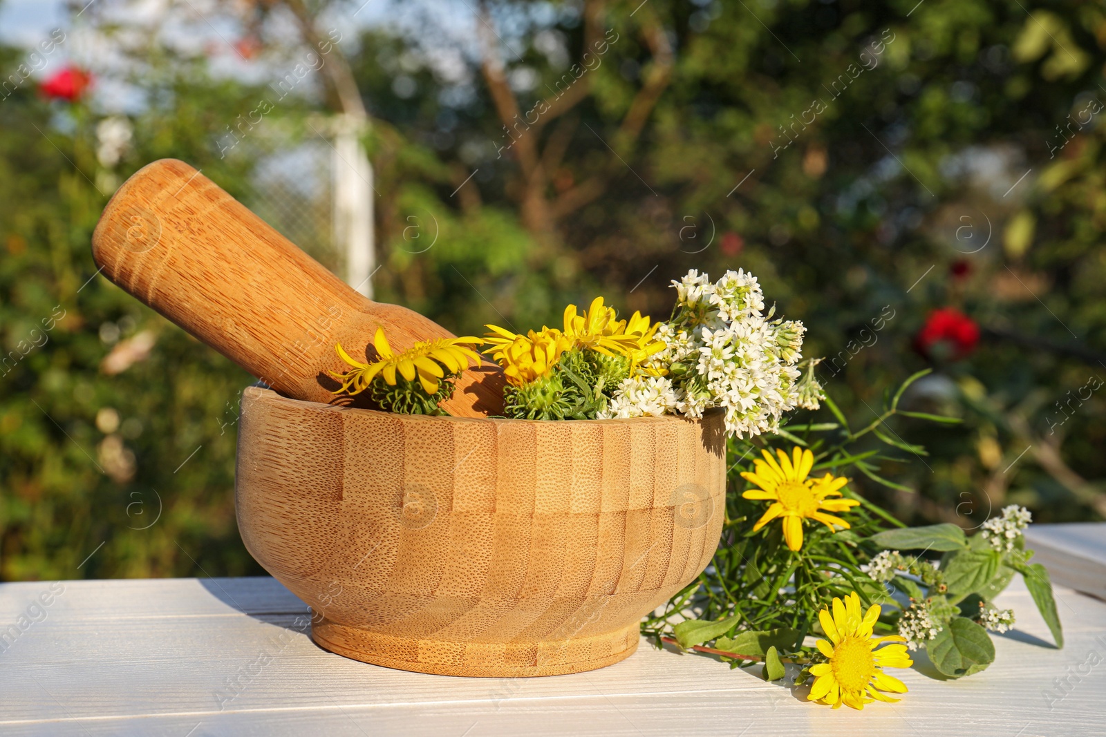 Photo of Mortar with pestle, flowers and herbs on white wooden table outdoors