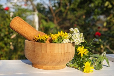 Photo of Mortar with pestle, flowers and herbs on white wooden table outdoors