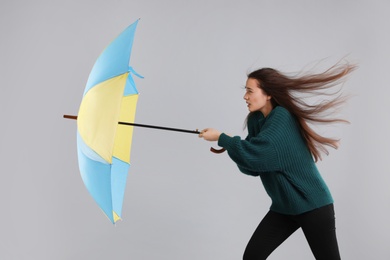 Photo of Woman with umbrella caught in gust of wind on grey background
