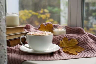 Photo of Cup of tasty hot drink with marshmallows near books, leaves and burning candle on blanket. Autumn coziness