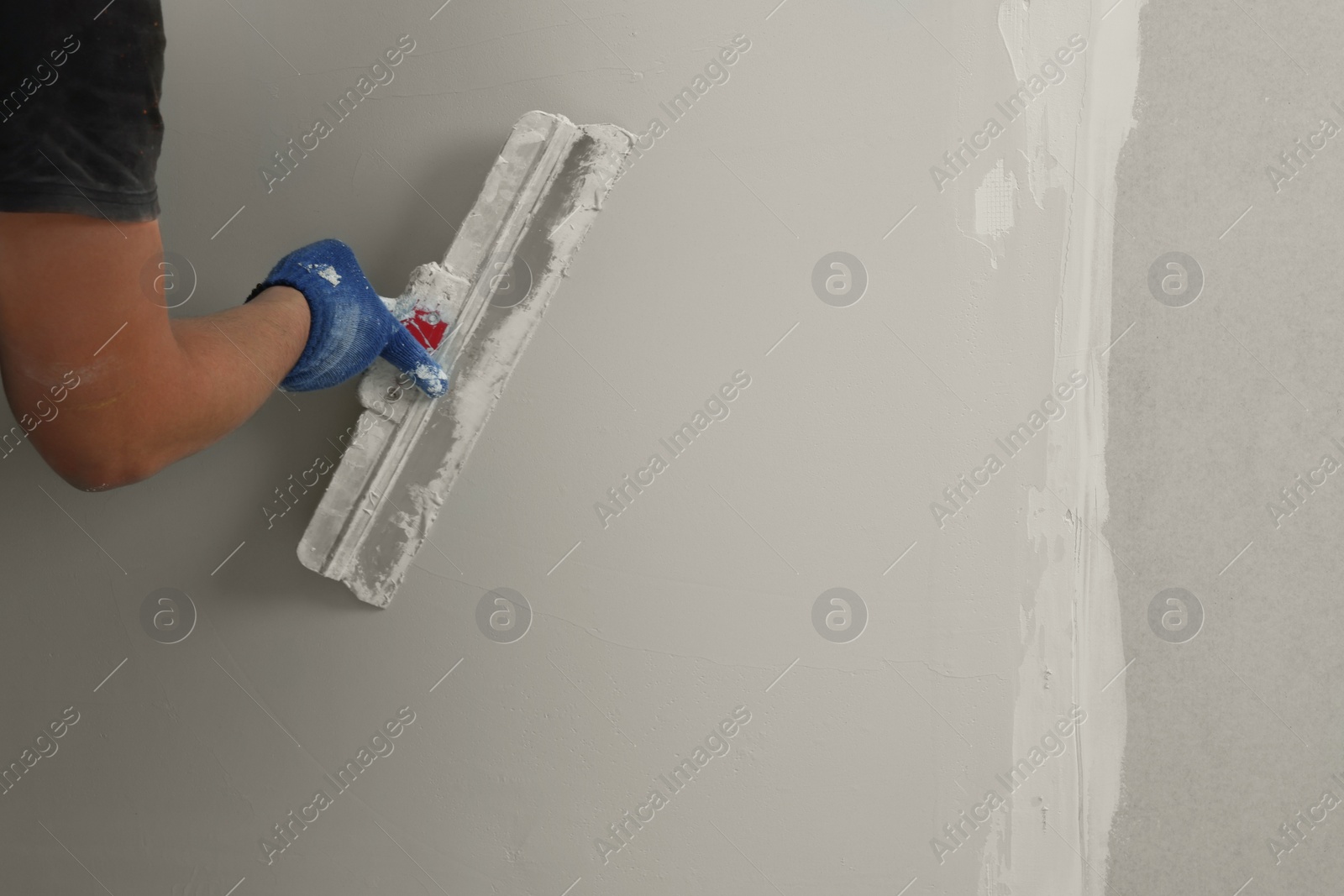 Photo of Professional worker plastering wall with putty knife, closeup