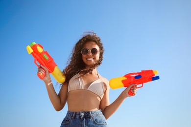 Photo of African American woman with water guns against blue sky, low angle view
